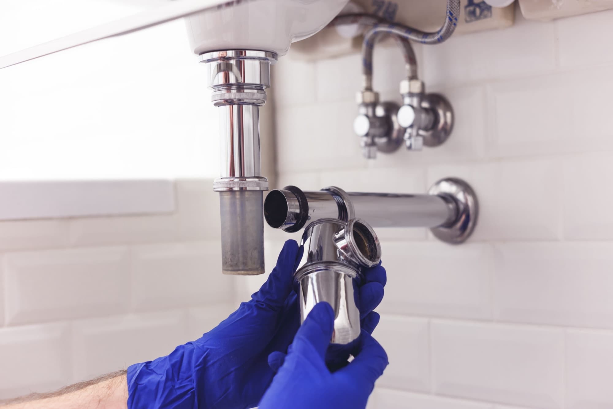 Plumber in blue gloves fitting a chrome sink drain trap