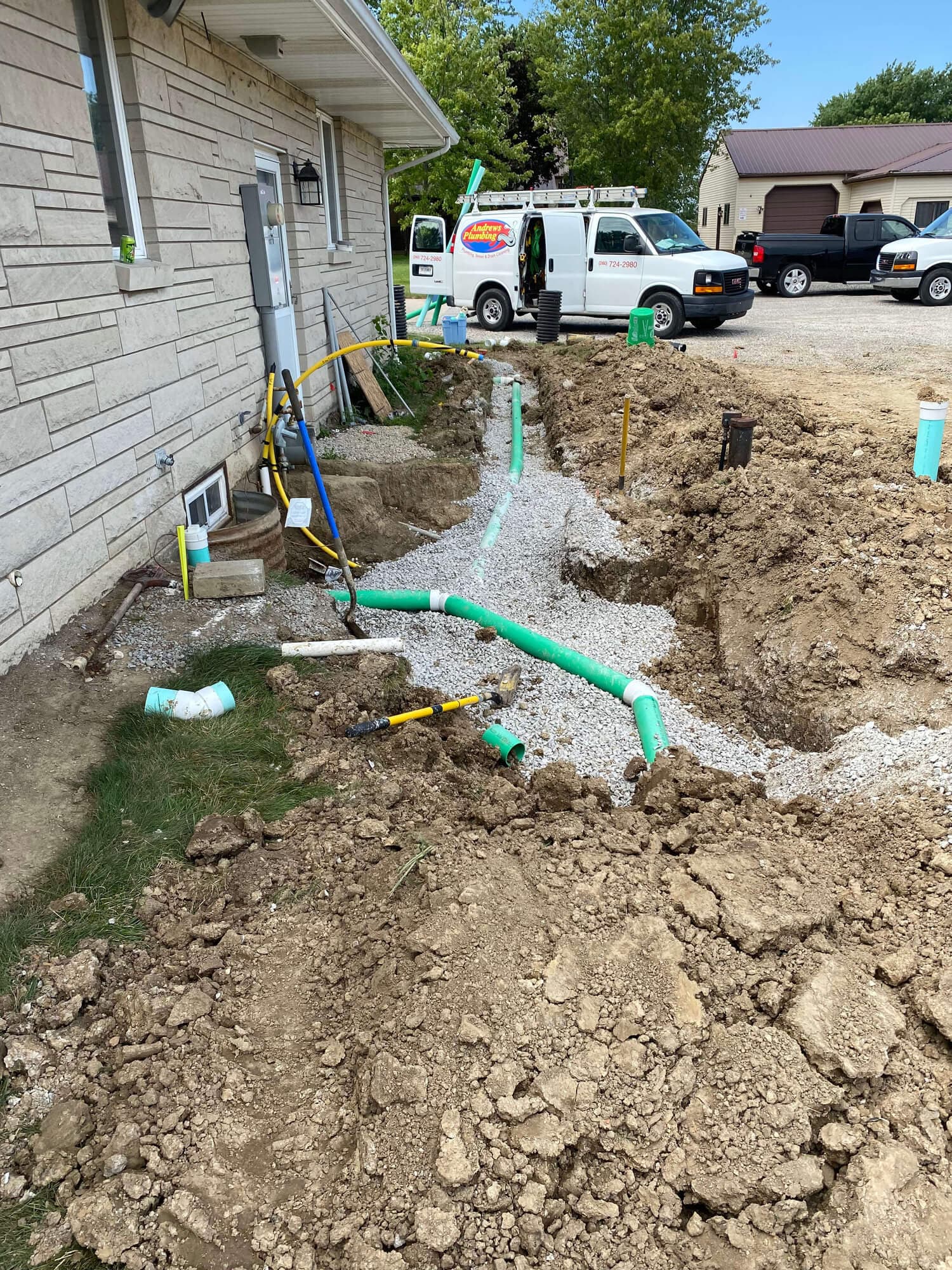 Andrews Plumbing sewer line excavation beside a home, with company trucks parked behind